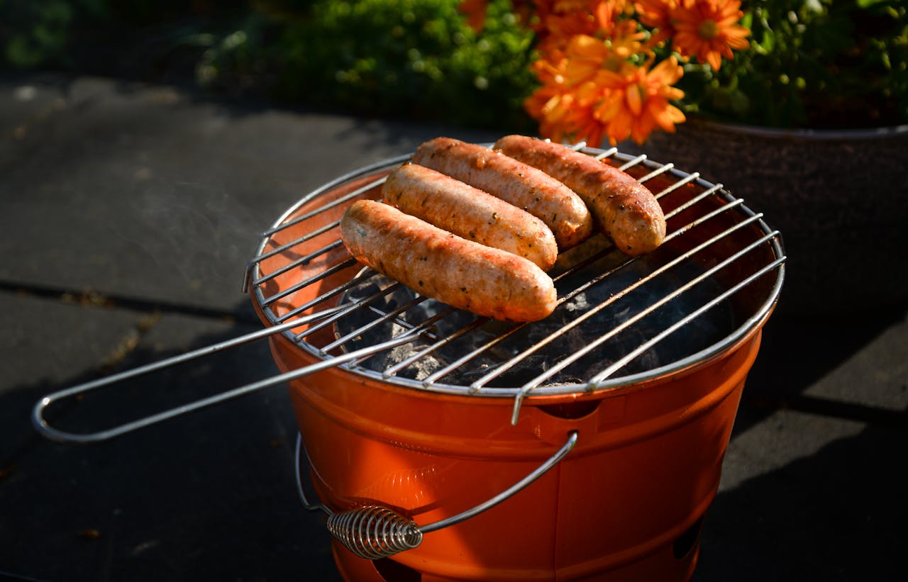 Four delicious sausages sizzling on a portable charcoal grill, ideal for summer picnics.