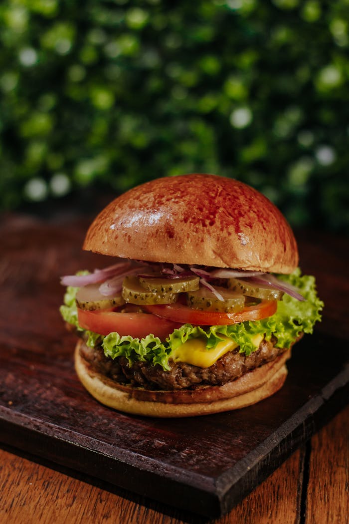 Juicy gourmet burger with fresh vegetables and cheese on a wooden board.