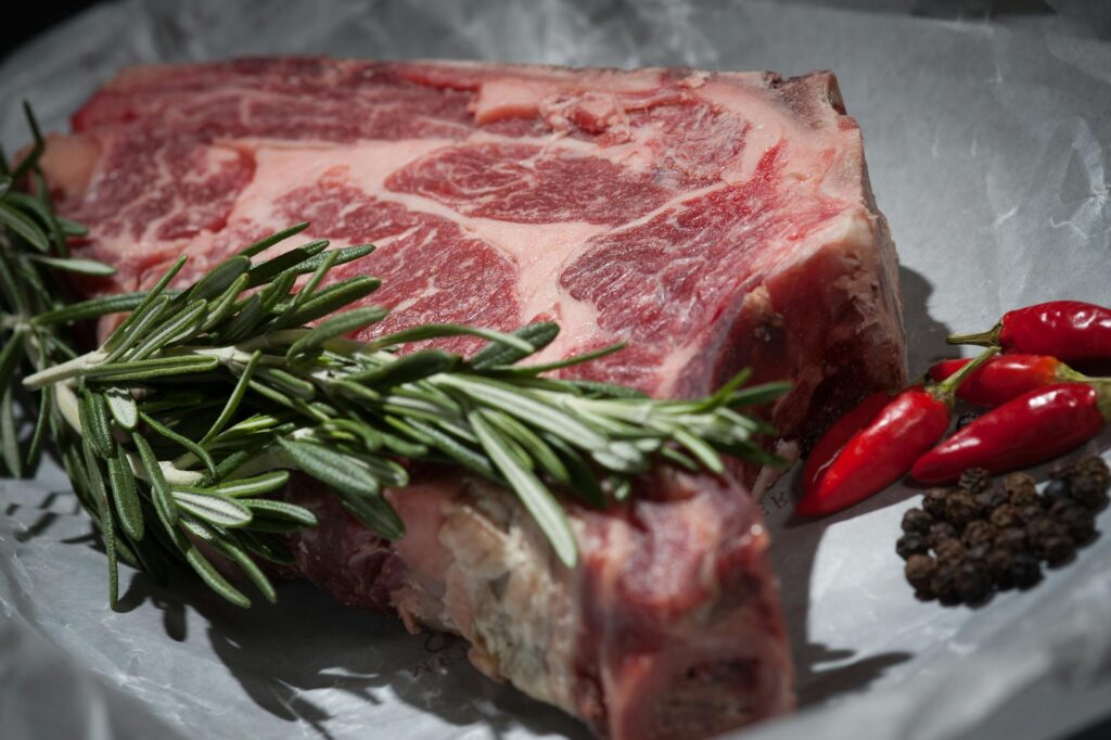 Close-up of a raw steak garnished with rosemary and chilies, ideal for cooking concepts.